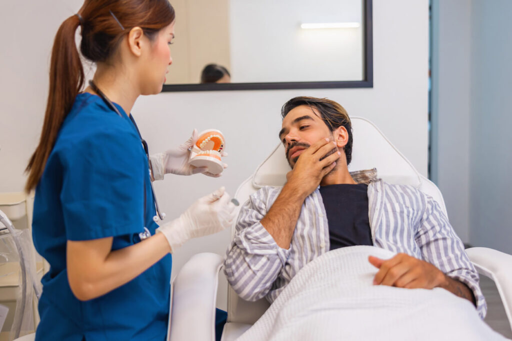difference between tmj and tmd explained as a dentist shows a jaw model to a patient touching his jaw in a dental clinic